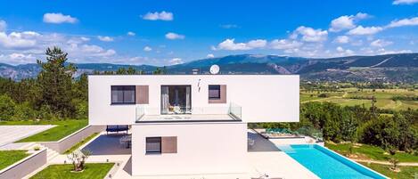 A modern two-story house with a swimming pool, surrounded by a well-maintained lawn and a scenic mountain view.