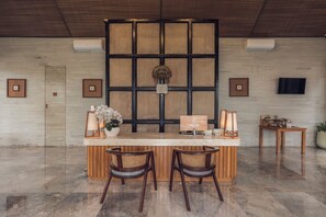 Una zona de recepción con mostrador de madera, dos sillas de mimbre, un panel decorativo y un televisor.