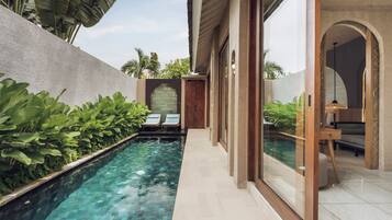 A swimming pool with a clear blue water surface, surrounded by lush green plants and a stone wall.