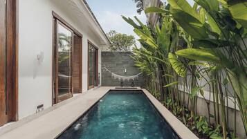 Una piscina con pared de piedra y plantas tropicales.
