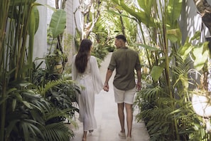 Una pareja camina de la mano por un estrecho sendero rodeado de exuberante vegetación.