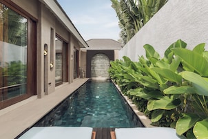 A modern building with a swimming pool, large windows, and tropical plants.