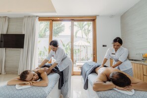 A massage therapy room with two massage tables, a TV, and a view of the outdoors. - Astera Villa Seminyak by Ini Vie Hospitality (Legian)