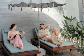 Dos sillones de descanso bajo un dosel, una terraza de madera y una planta en maceta.