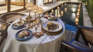 An outdoor dining area with a pool, surrounded by a modern house with large windows and a well-lit interior. - Astera Villa Seminyak by Ini Vie Hospitality (Legian)
