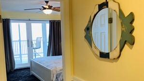 Un dormitorio con cama, ventilador de techo, ventana con cortinas y puerta que da a un balcón.