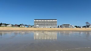 Hotel frente al mar con varios pisos, una playa en primer plano y un cielo despejado.