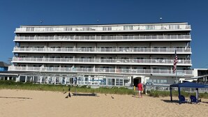 Un hotel de varios pisos con balcones, vista a la playa y una bandera.