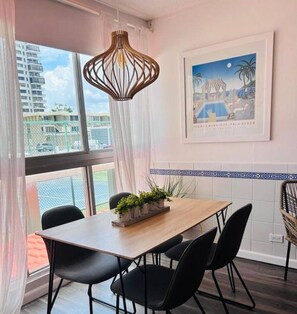 Un coin repas avec une table en bois, des chaises noires, un luminaire suspendu, une plante en pot et un tableau encadré au mur.