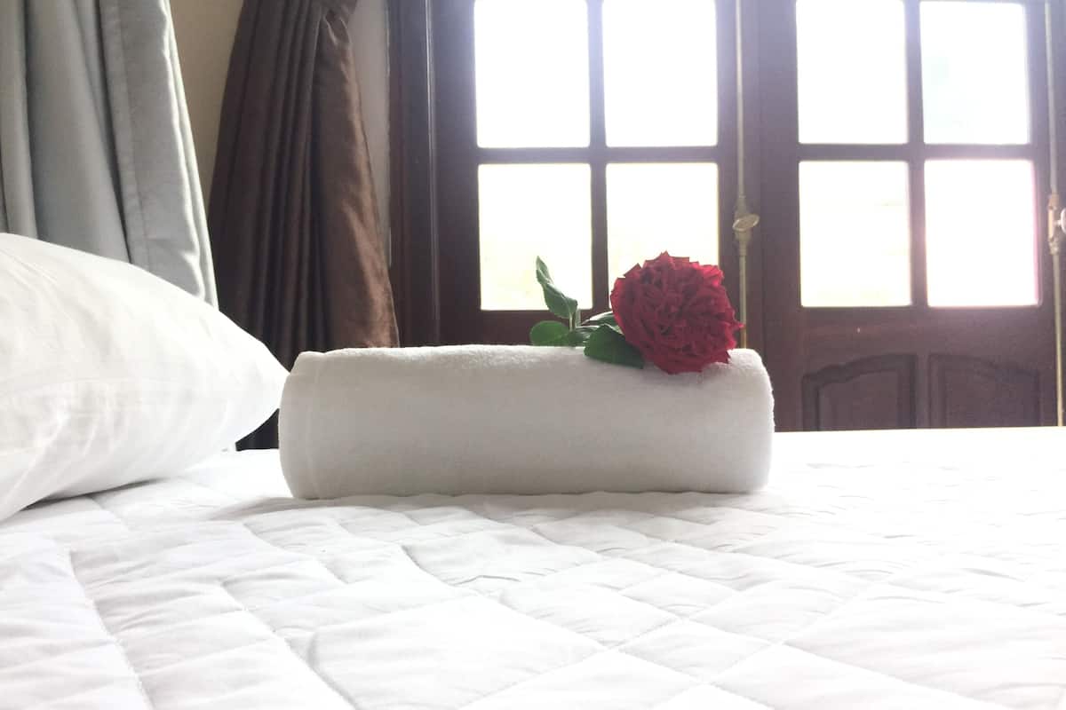 A neatly made bed with a rolled white towel and a red rose on top.