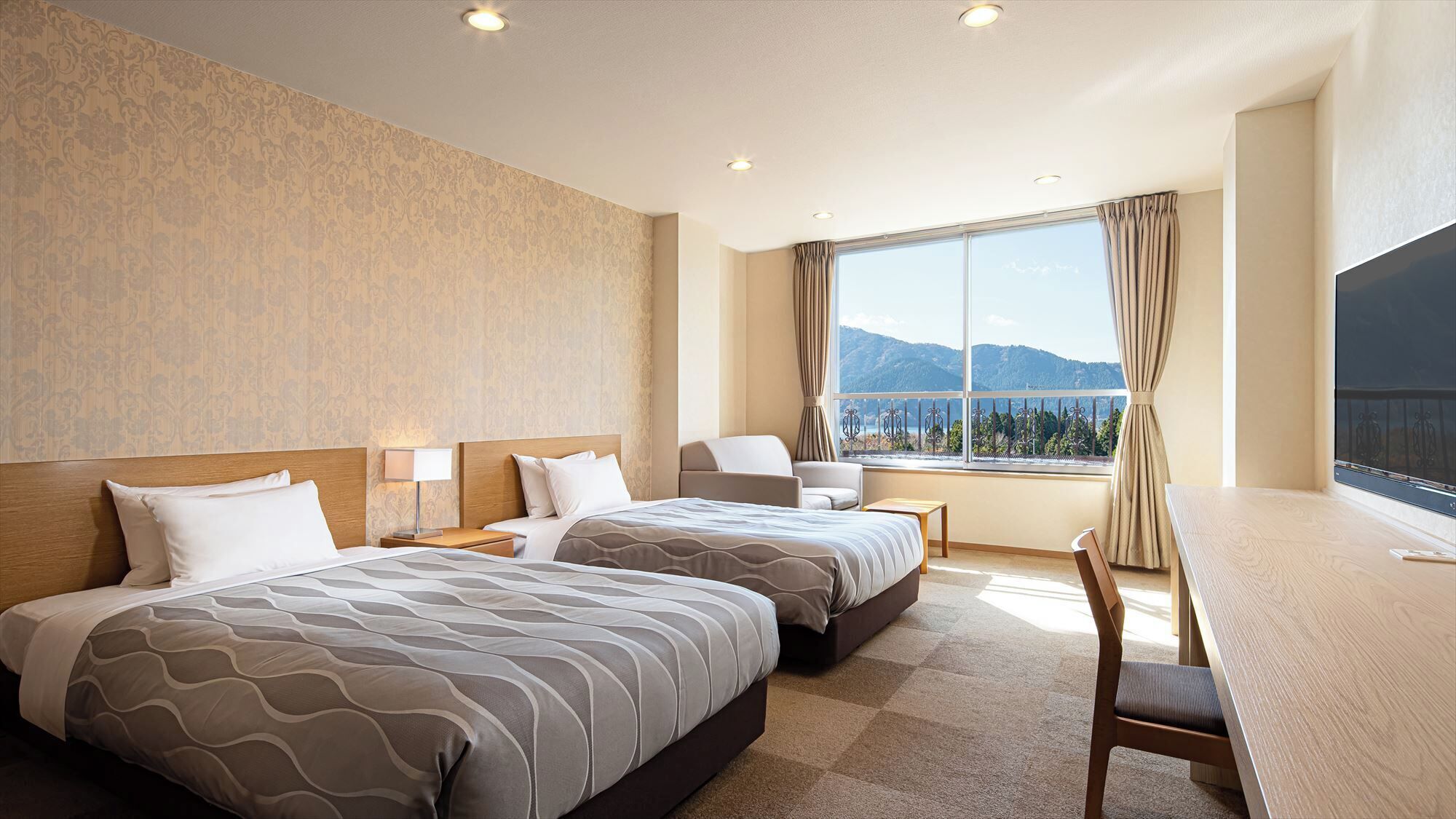 A hotel room with two beds, a desk, a chair, and a large window with a view of mountains.