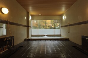 Un bain public offrant une vue sur le feuillage automnal grâce à de grandes fenêtres, avec des murs carrelés et un plafond en bois.