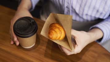 A person holding a paper bag with a croissant and a coffee cup.