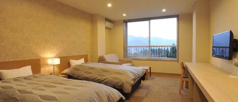 A hotel room with two beds, a desk, a chair, a TV, and a large window with a mountain view.