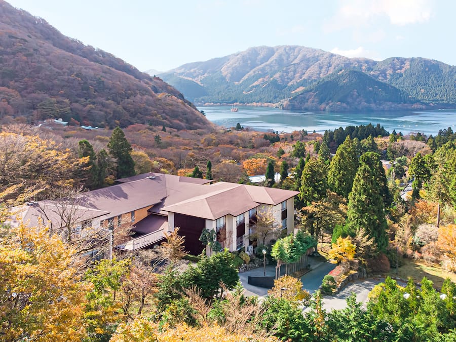A house with a sloped roof, surrounded by autumn foliage and mountains in the background.