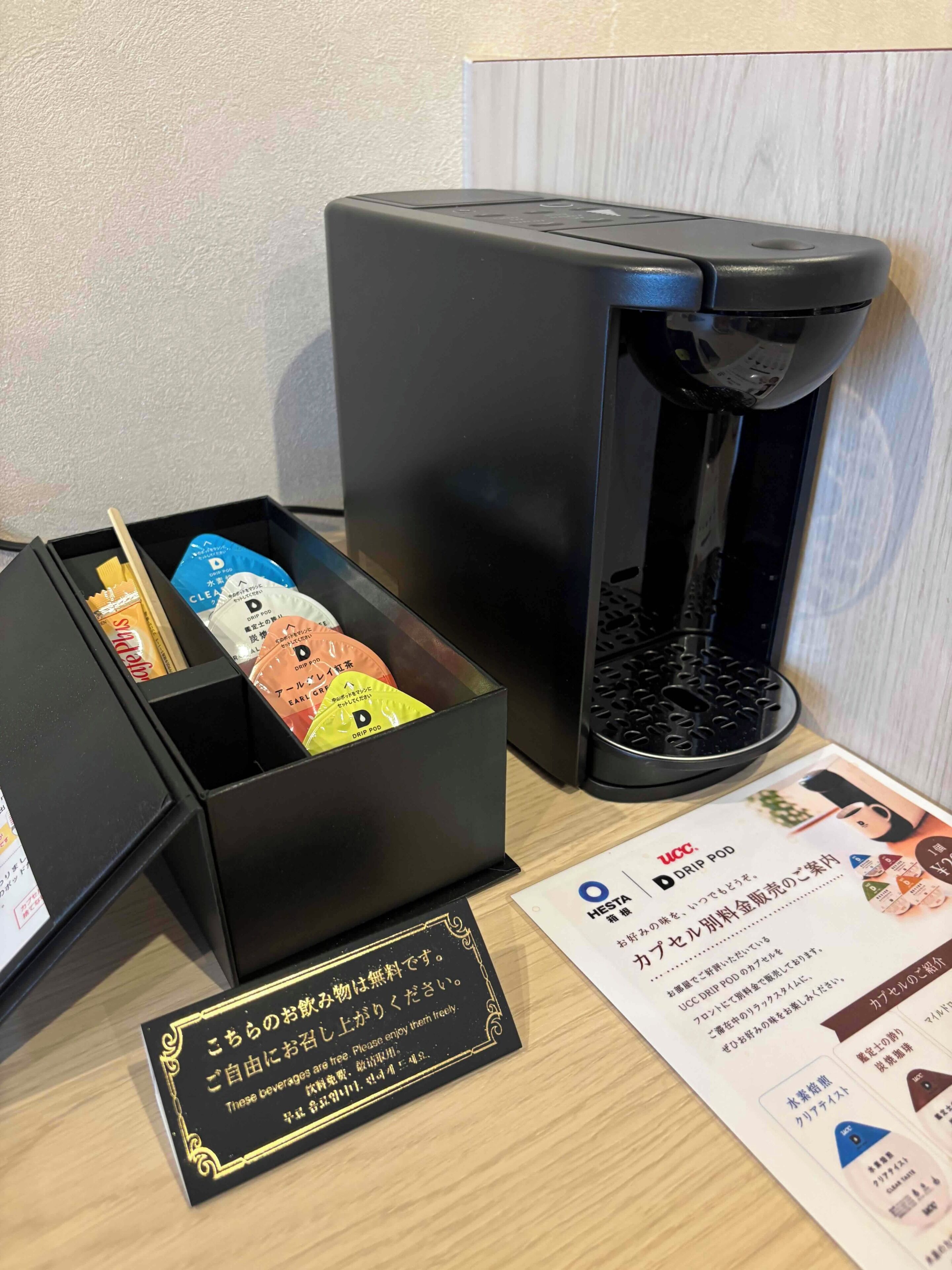 A drip coffee maker with a black box containing coffee pods and a card with Japanese text.