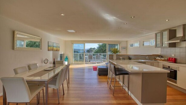 A modern kitchen with a central island, dining area with chairs, and a view to the outdoors.