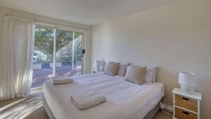 A bedroom with a large bed, a nightstand, a lamp, and a view of the outdoors through a sliding door.