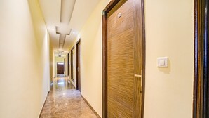 A hotel hallway with wooden doors, a marble floor, and a light switch on the wall. - FabHotel Diamond (Dera Bassi)