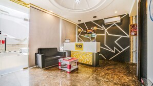 A hotel reception area with a modern design, including a reception desk, a sofa, a small table, and a patterned wall. - FabHotel Diamond (Dera Bassi)