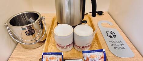 A coffee station with a kettle, two mugs, a tray with coffee packets, and a sign indicating the room.