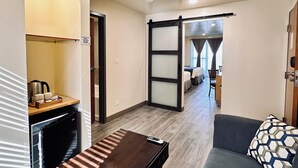Ein Hotelzimmer mit Schiebetür zu einem Schlafbereich, einer kleinen Küchenzeile, einem Sofa und einem Schreibtisch mit Stuhl.