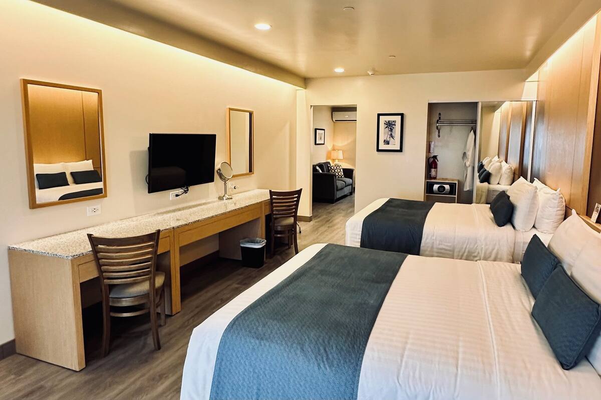 Habitación de hotel con dos camas, un escritorio, una silla, un televisor y un espejo.