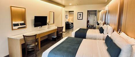 Quarto de hotel com duas camas, uma escrivaninha, uma cadeira, uma televisão e um espelho.