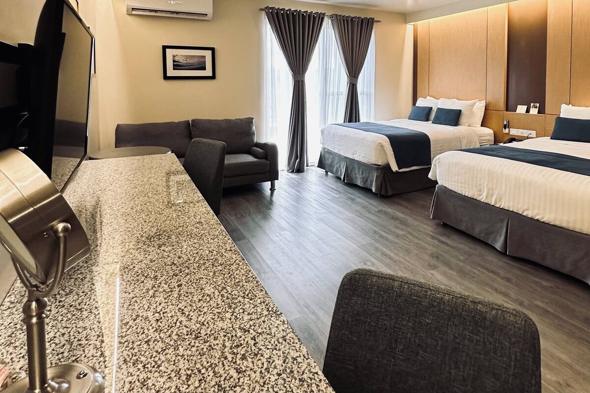 Una habitación de hotel con una cama grande, una cama más pequeña, un sofá, un escritorio y un televisor.