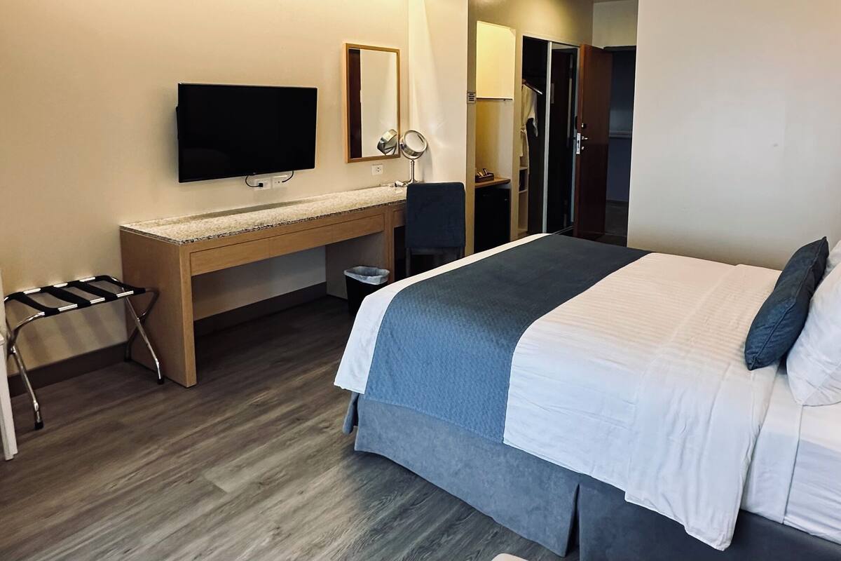 Una habitación de hotel con cama, escritorio, televisor, espejo y armario.