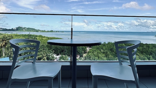 Ein Balkon mit zwei weißen Stühlen und einem kleinen runden Tisch, mit Blick auf eine malerische Wassersicht und entfernte Landstriche.