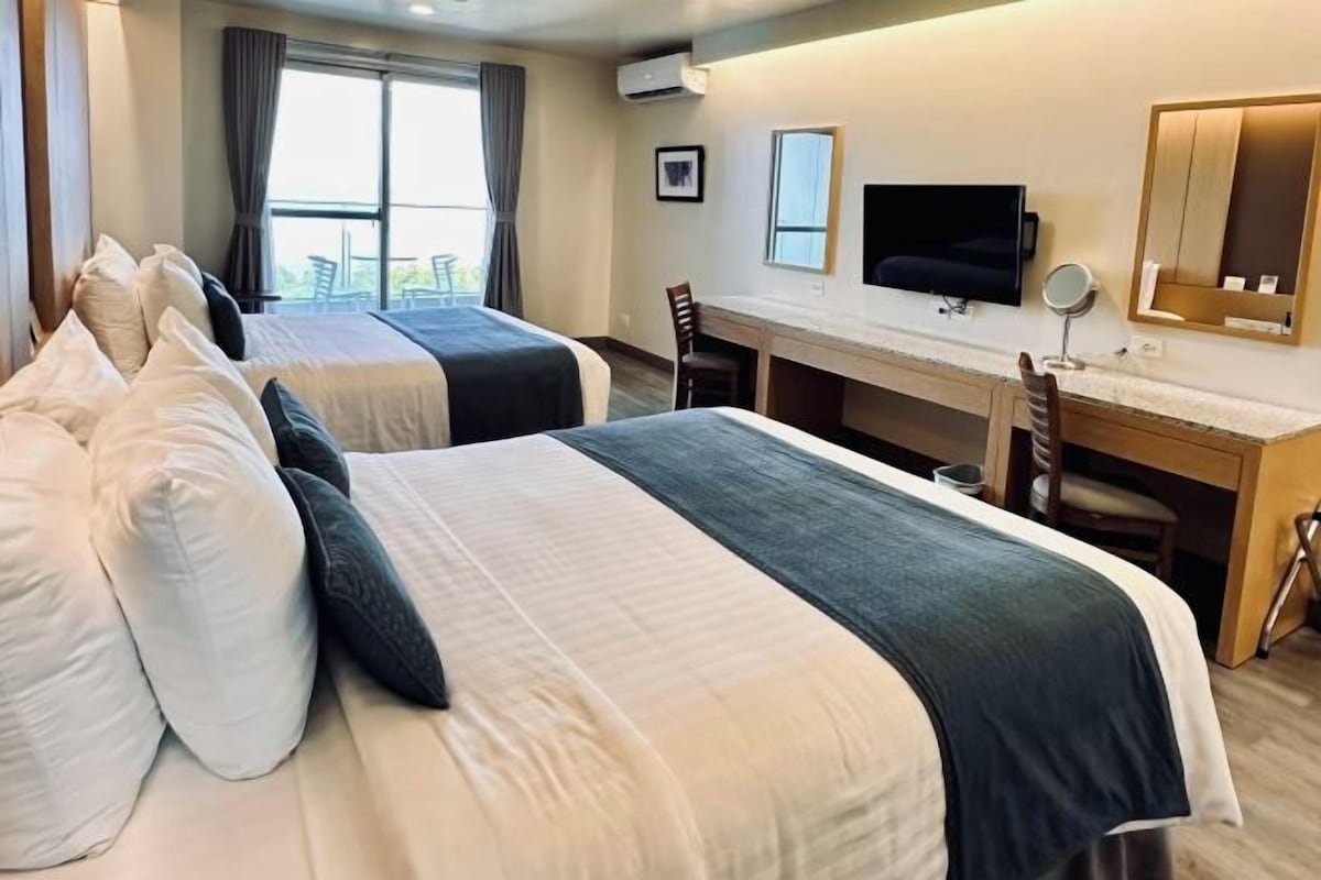 Habitación de hotel con dos camas, un escritorio, una silla, un televisor y una ventana con cortinas.
