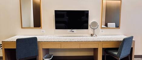 A hotel room with a wooden desk, two chairs, a TV, and two wall-mounted mirrors.