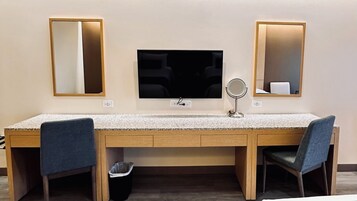 Habitación de hotel con un escritorio de madera, dos sillas, un televisor y dos espejos en la pared.