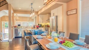 A spacious dining area with a long wooden table set for a meal, modern lighting fixtures, and a view into the kitchen area.