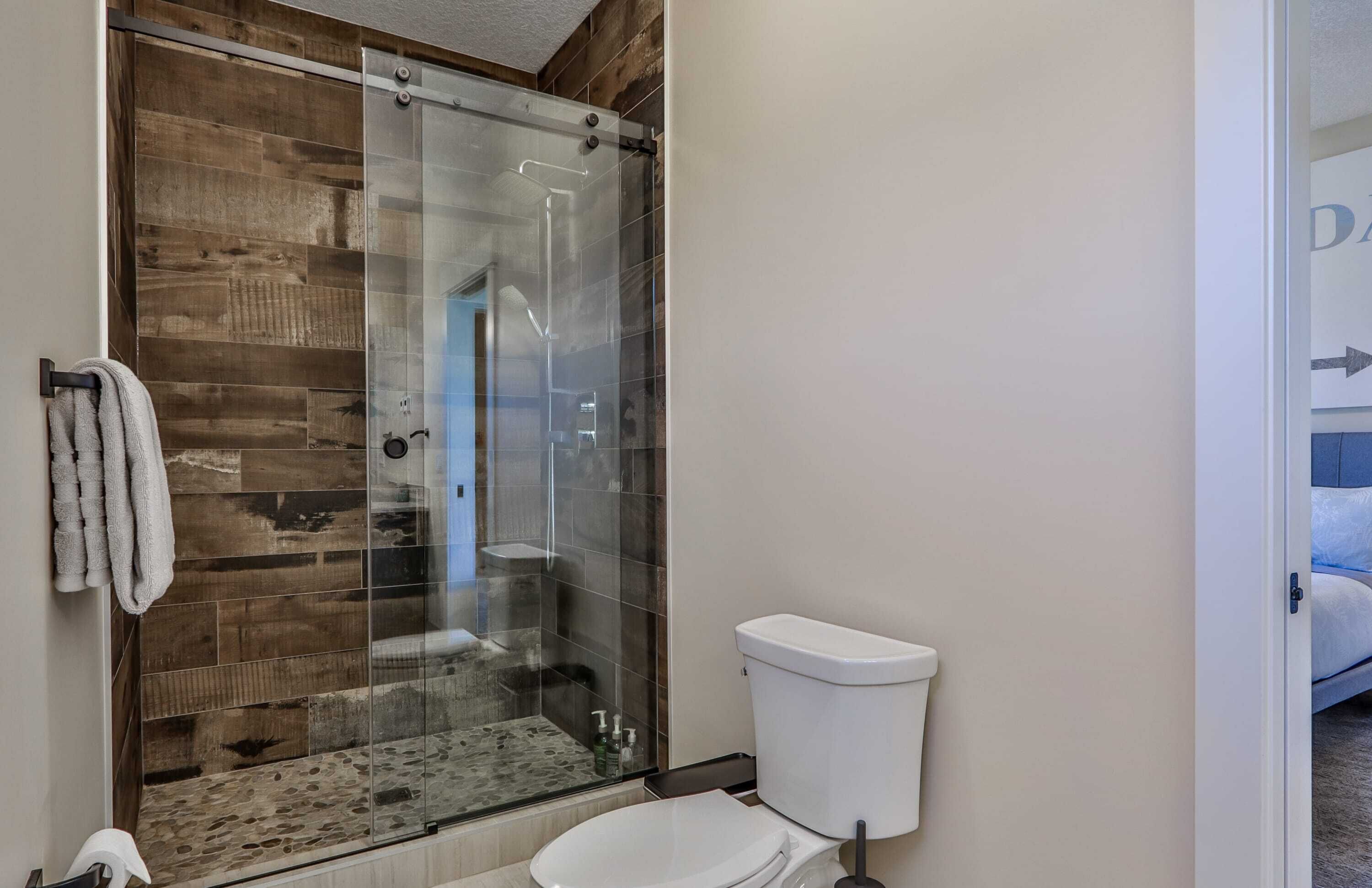 A bathroom with a glass-enclosed shower, a white toilet, and a towel hanging on the wall.