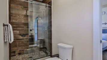 A bathroom with a glass-enclosed shower, a white toilet, and a towel hanging on the wall.