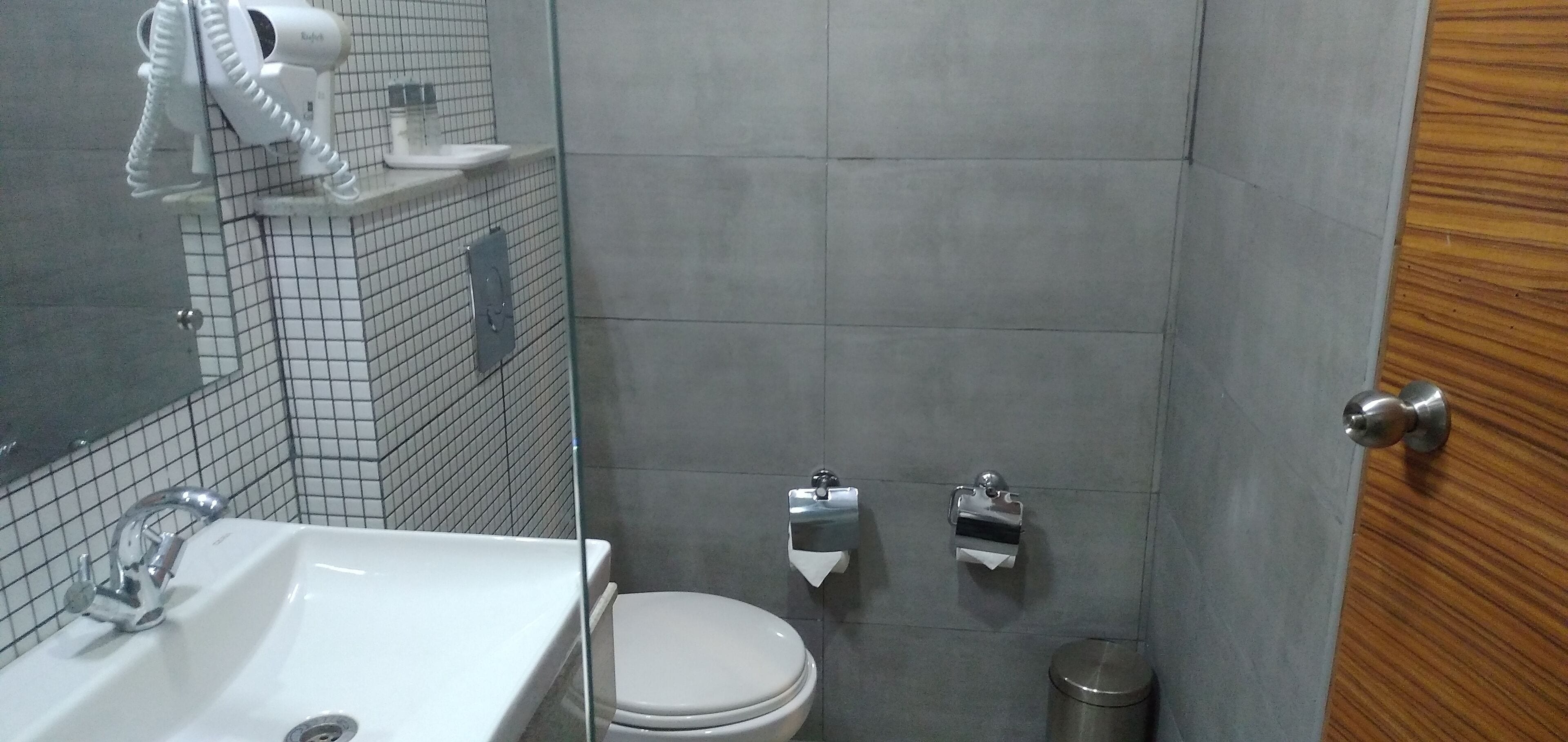 Une salle de bain avec un lavabo blanc, des toilettes, un sèche-mains et une poubelle.