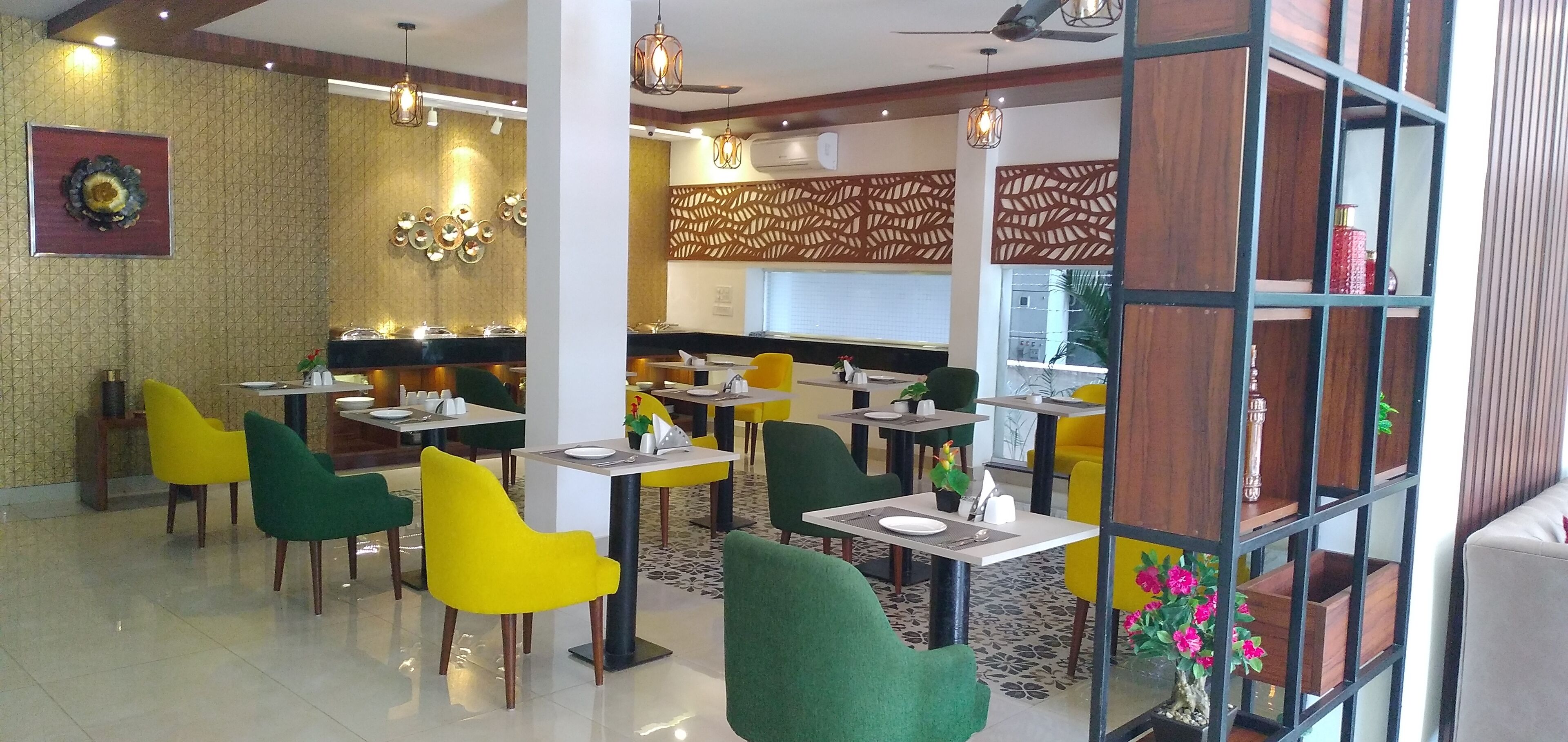 A modern restaurant with green and yellow chairs, a decorative wall, and a ceiling fan.