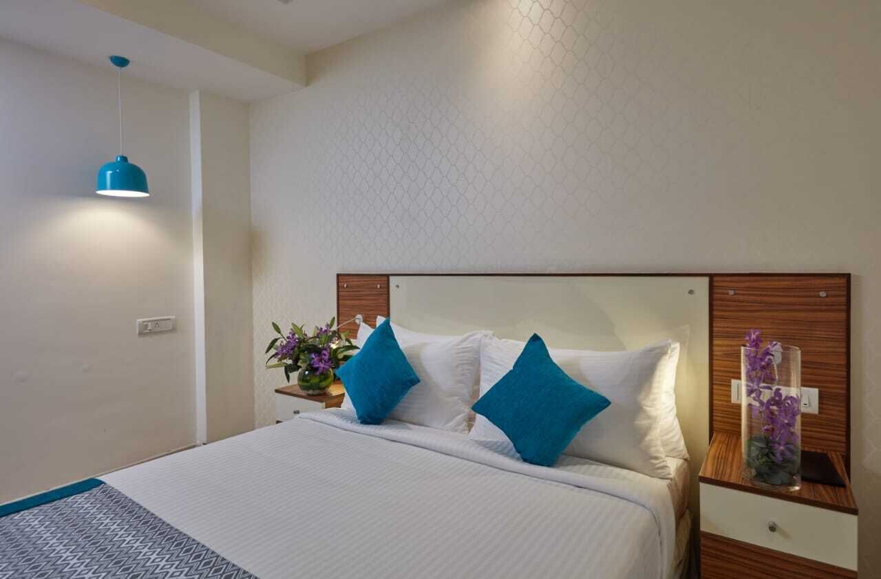 A neatly made bed with blue and white pillows, a bedside table with a vase of flowers, and a hanging blue pendant light.
