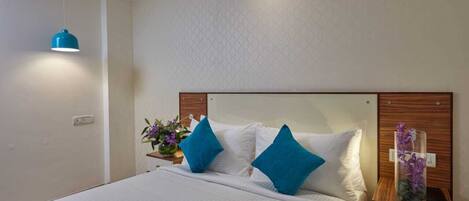 A neatly made bed with blue and white pillows, a bedside table with a vase of flowers, and a hanging blue pendant light.
