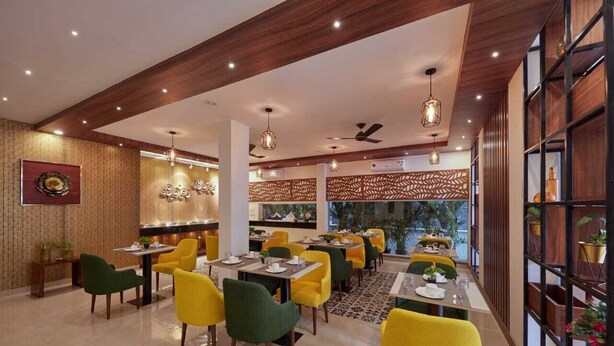 Restaurante com cadeiras amarelas e verdes, vigas de madeira no teto e parede com padrão.
