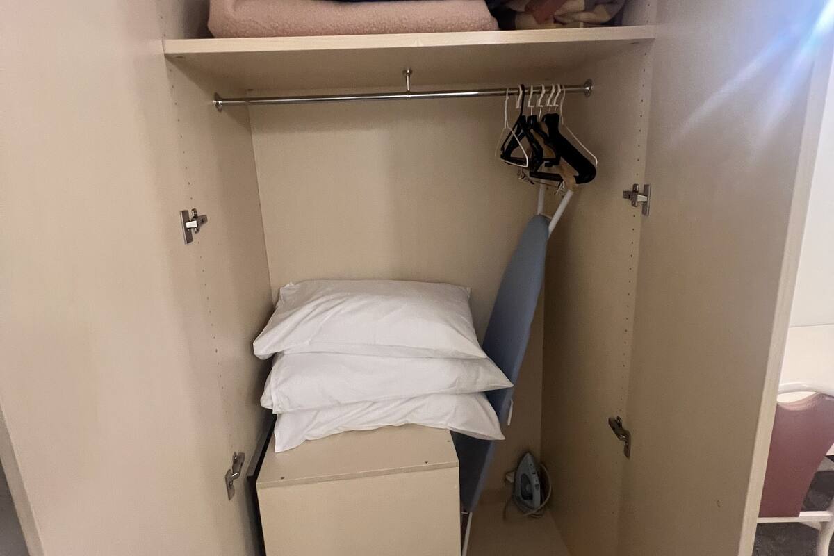 A compact storage unit with a shelf, hanging rack, and a folded blanket.