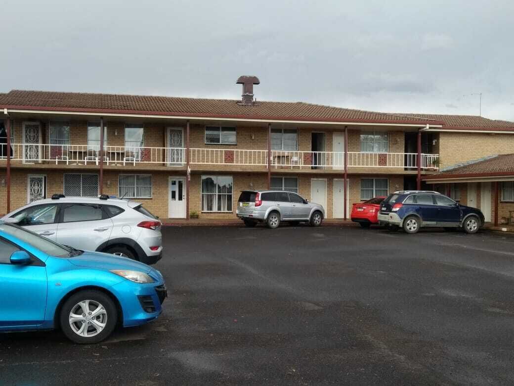 Un motel composé d’un bâtiment à deux étages, d’un parking avec plusieurs voitures et d’un balcon situé à l’étage supérieur.