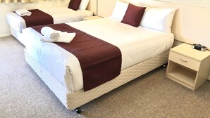 A hotel room with two beds, each with white linens and brown headboards. There is a beige carpet, a small bedside table with a lamp, and a wall-mounted clock. - Overlander Motor Lodge (Gunnedah)