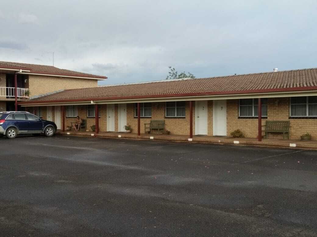 A motel with a row of rooms, a covered parking area, and a car parked in front.
