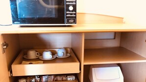 A compact kitchenette with a microwave, tea set, toaster, and storage containers. - Overlander Motor Lodge (Gunnedah)