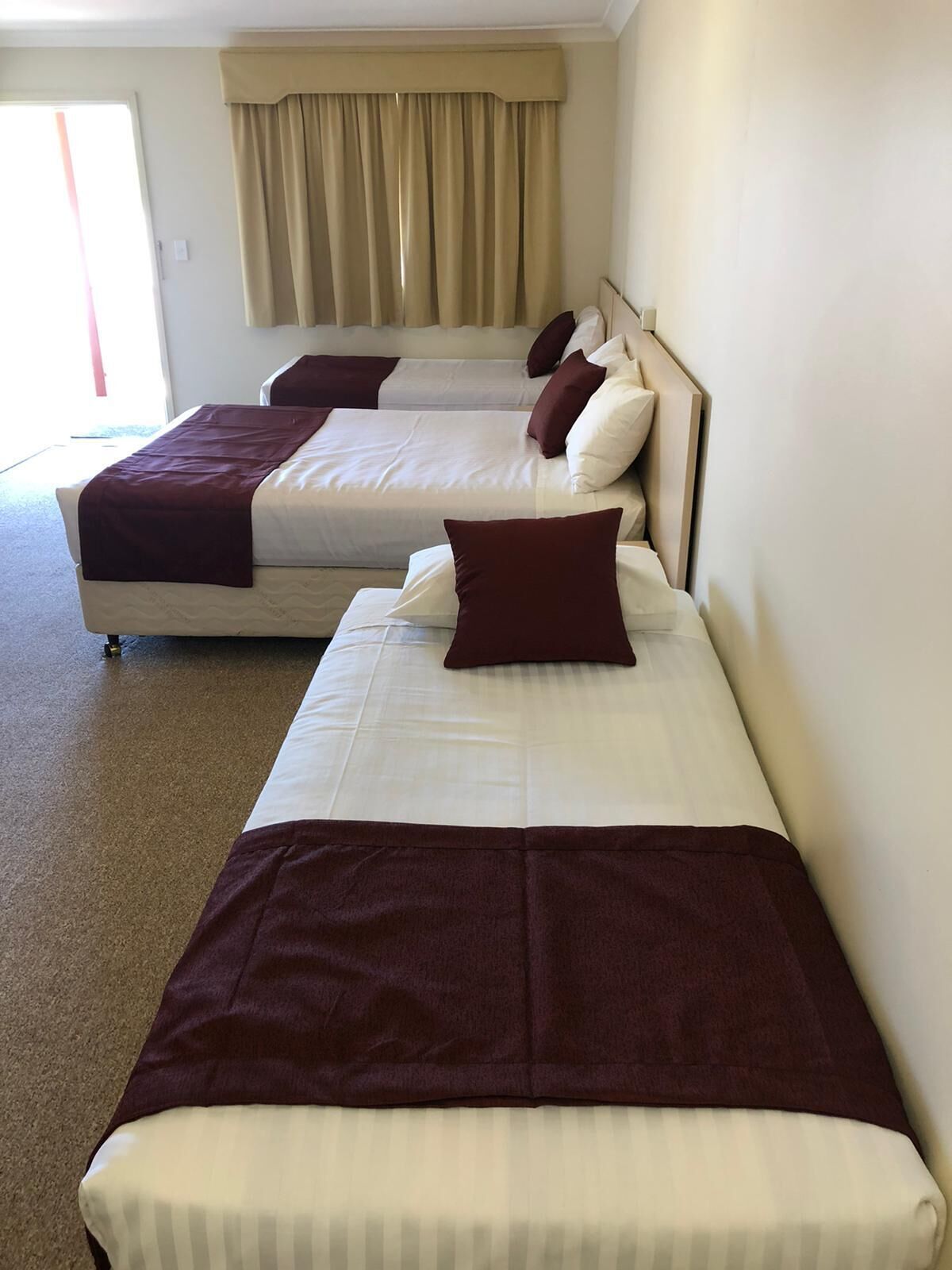 Habitación de hotel con dos camas, cortinas color beige y vistas al exterior.