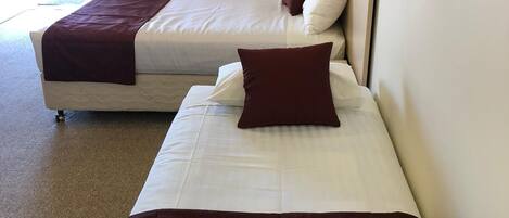 A hotel room with two beds, beige curtains, and a view of the outside.