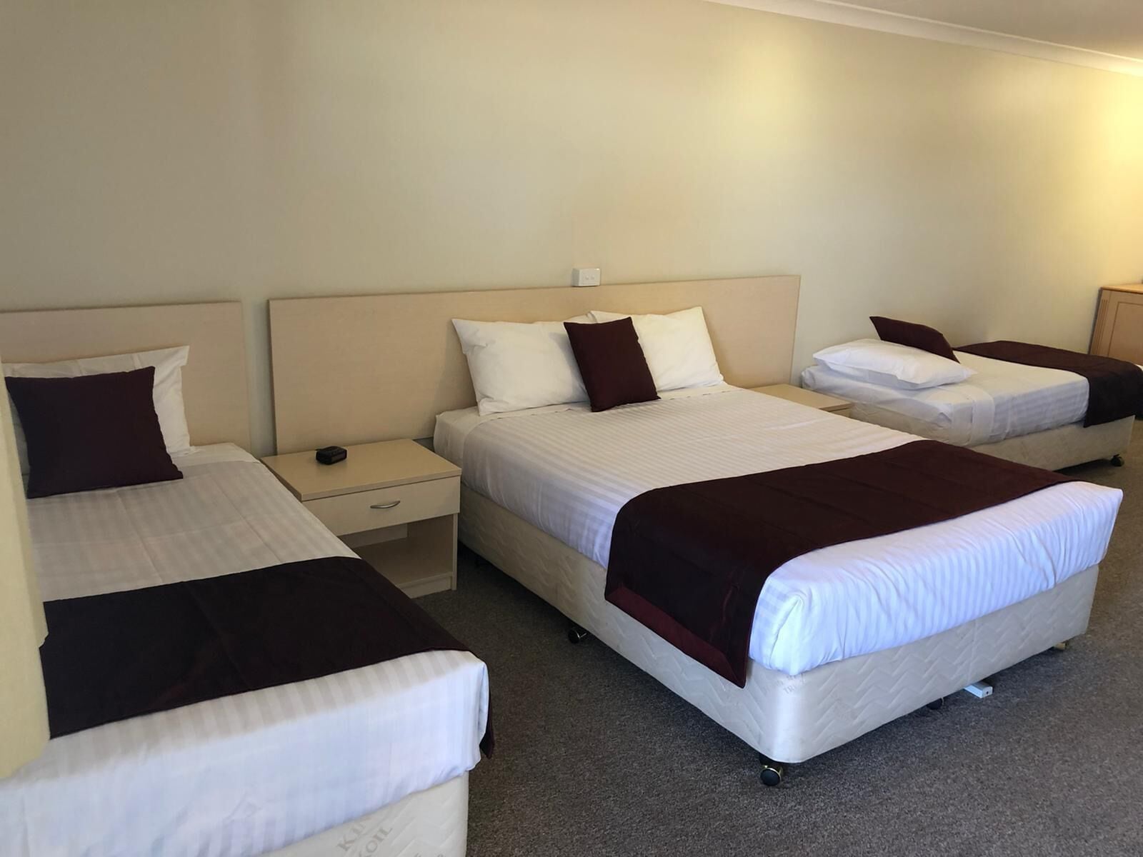 Une chambre d’hôtel avec trois lits alignés, chacun doté d’une tête de lit, de tables de chevet et d’un tiroir.